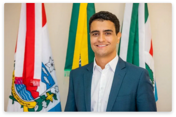 Foto mostra o prefeito João Henrique Caldas. Ele é branco, veste terno azul e camisa branca. Ele sorri. 