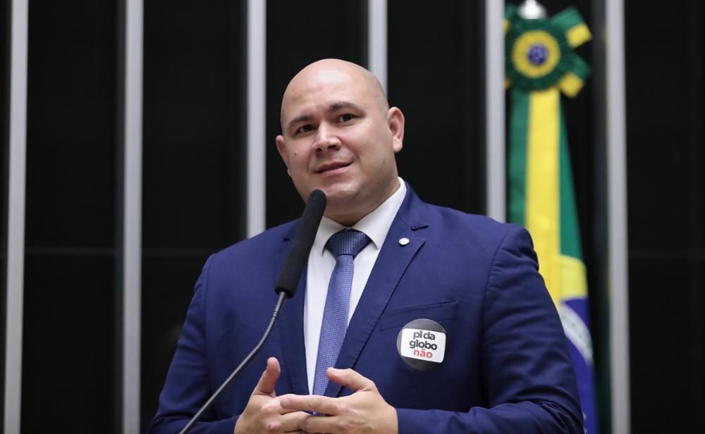 Abílio Brunini é branco, careca, veste terno azul escuro, camiseta branca e gravata roxa 