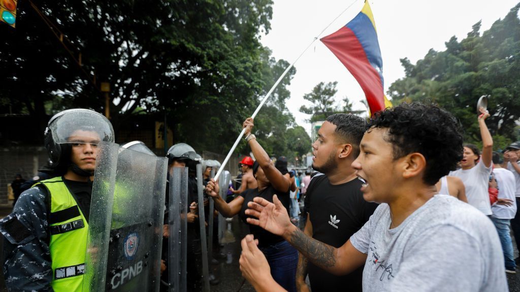 Manifestantes na Venezuela expressam sua raiva em frente a uma fileira de policiais durante um protesto contra os resultados oficiais da eleição presidencial