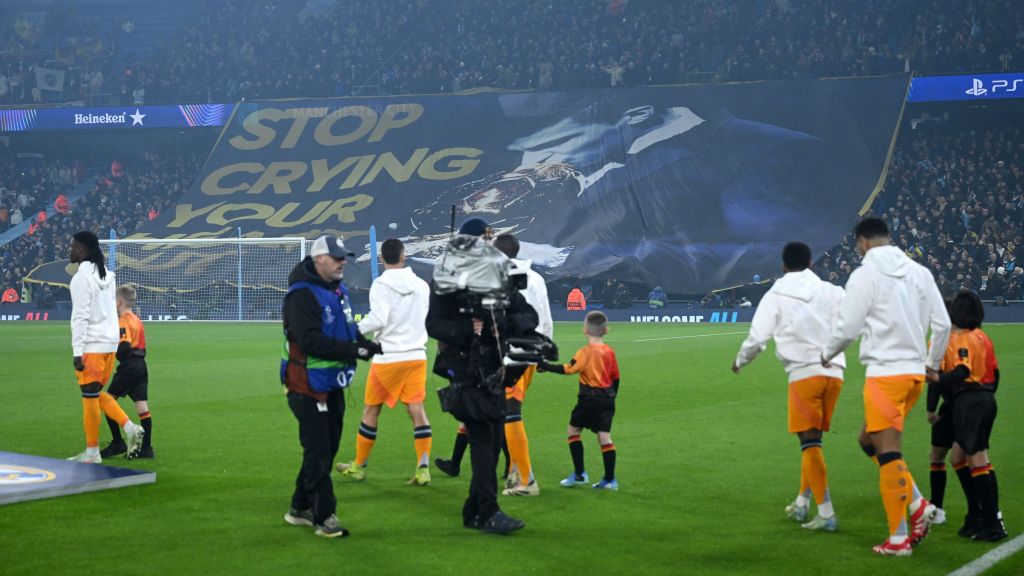 Real Madrid entra em campo no Etihad Stadium enquanto a torcida do Manchester City exibe bandeirão provocando Vini Jr