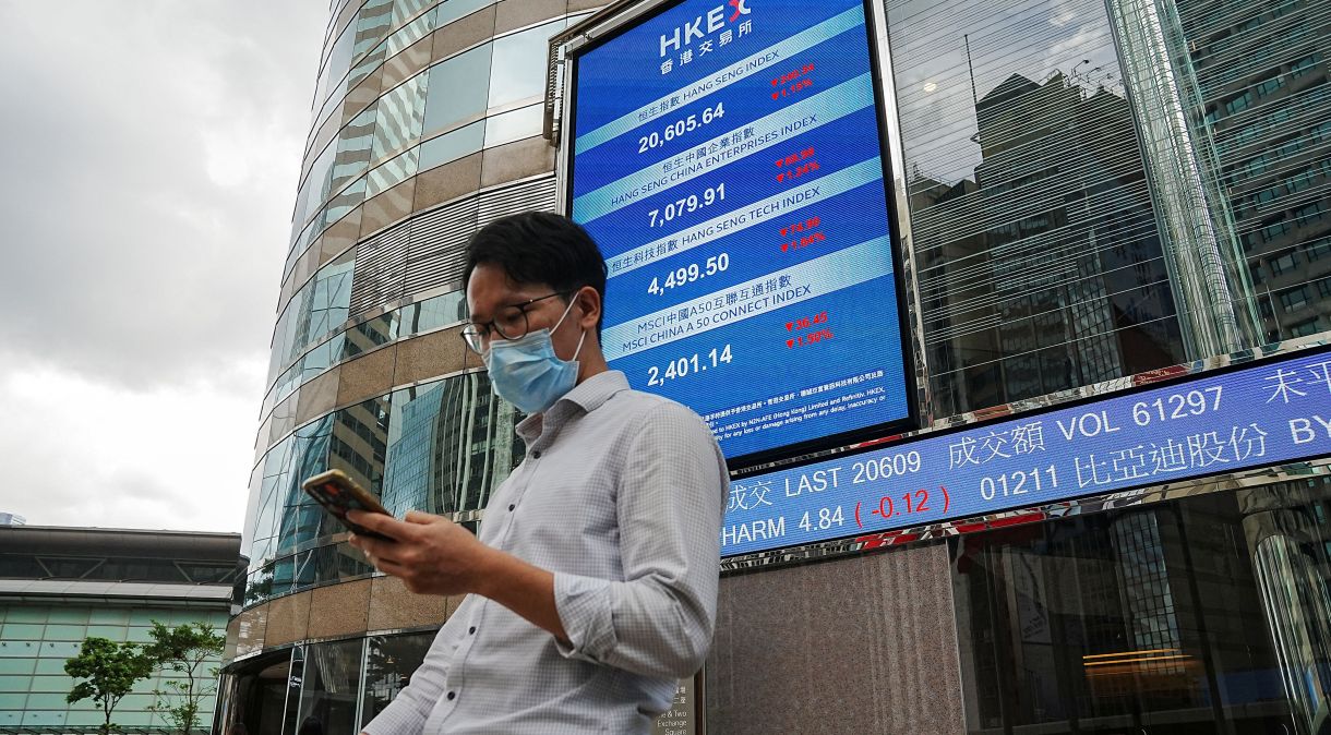 Pessoas passam em frente a tela mostrando cotações de ações na fachada do prédio da bolsa de Hong Kong