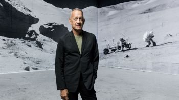 Imagens de arquivo de foguetes espaciais decolando são projetadas em paredes gigantes enquanto o ator de Hollywood narra a história das viagens humanas à Lua