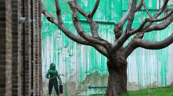 Obra inclui um estêncil, típico de Banksy, de uma pessoa segurando um dispositivo de pulverização, pingando tinta verde