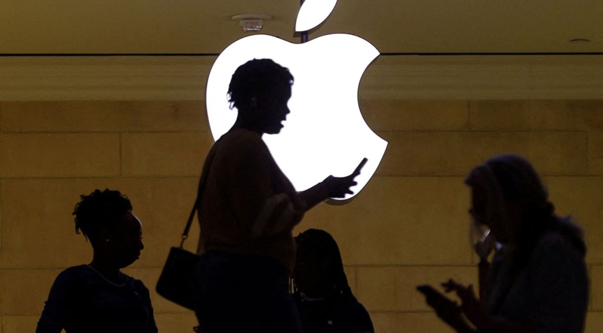 Mulher usa iPhone ao passar por logotipo iluminado da Apple em Nova York