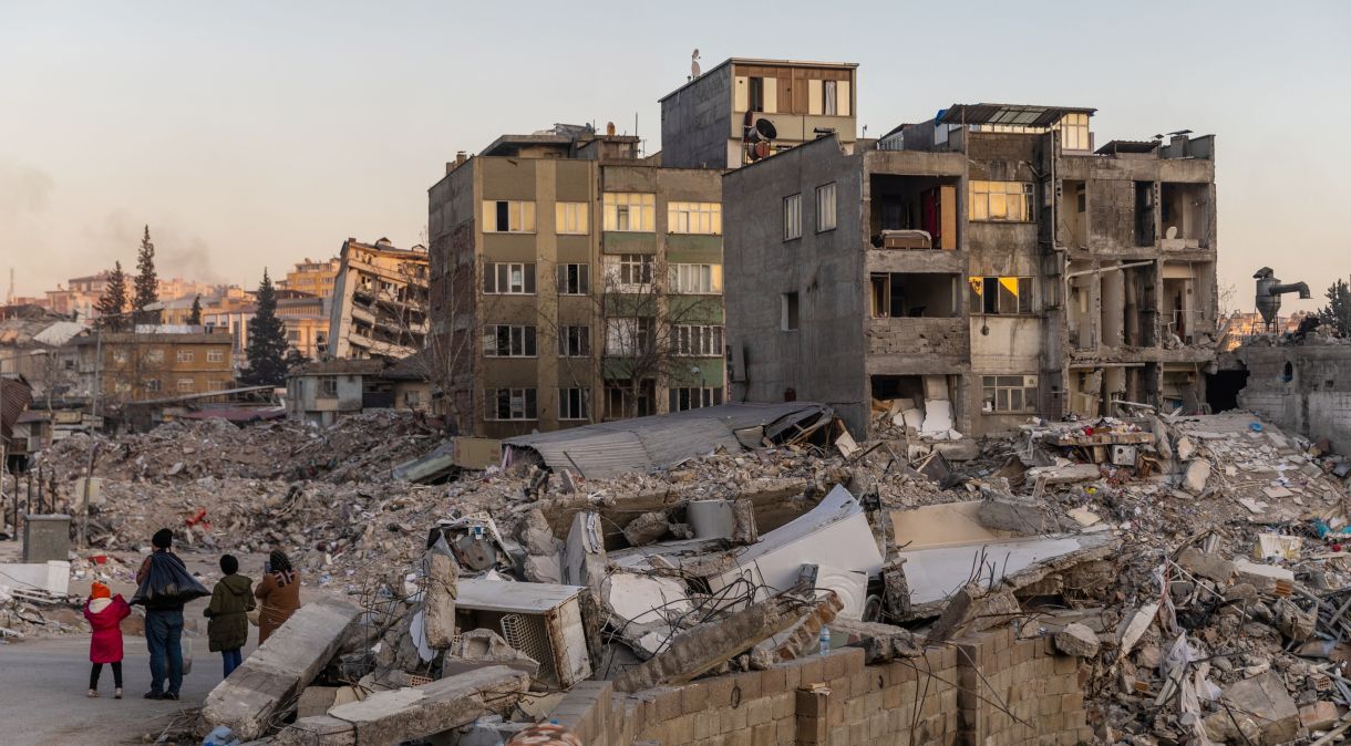 Pessoas olham para edifícios danificados e pilhas de escombros em Kahramanmaras, Turquia, após terremoto