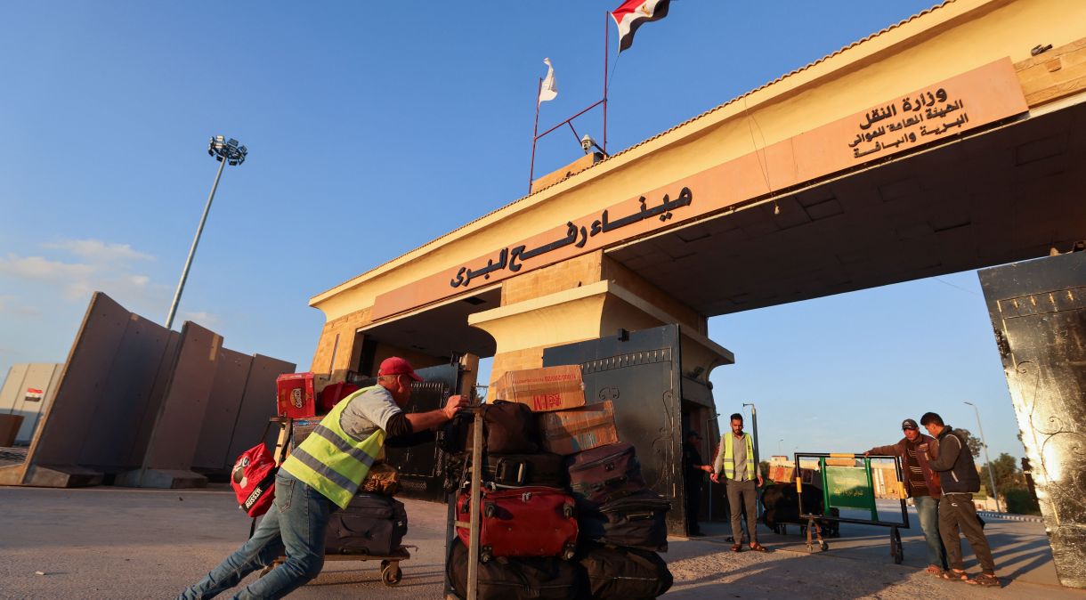 Trabalhador empurra carrinho de bagagem com pertences de palestinos que tentam voltar para Gaza, na passagem de fronteira de Rafah