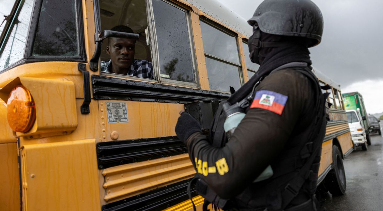 Um oficial da Polícia Nacional Haitiana para um ônibus em um posto de segurança em Limonade, Haiti