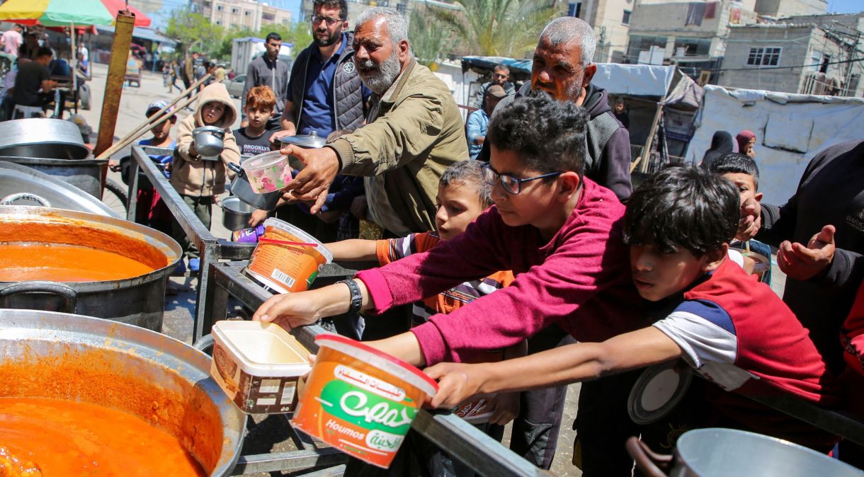 Grupo de palestinos recebe comida de uma organização humanitária em Rafah, Gaza