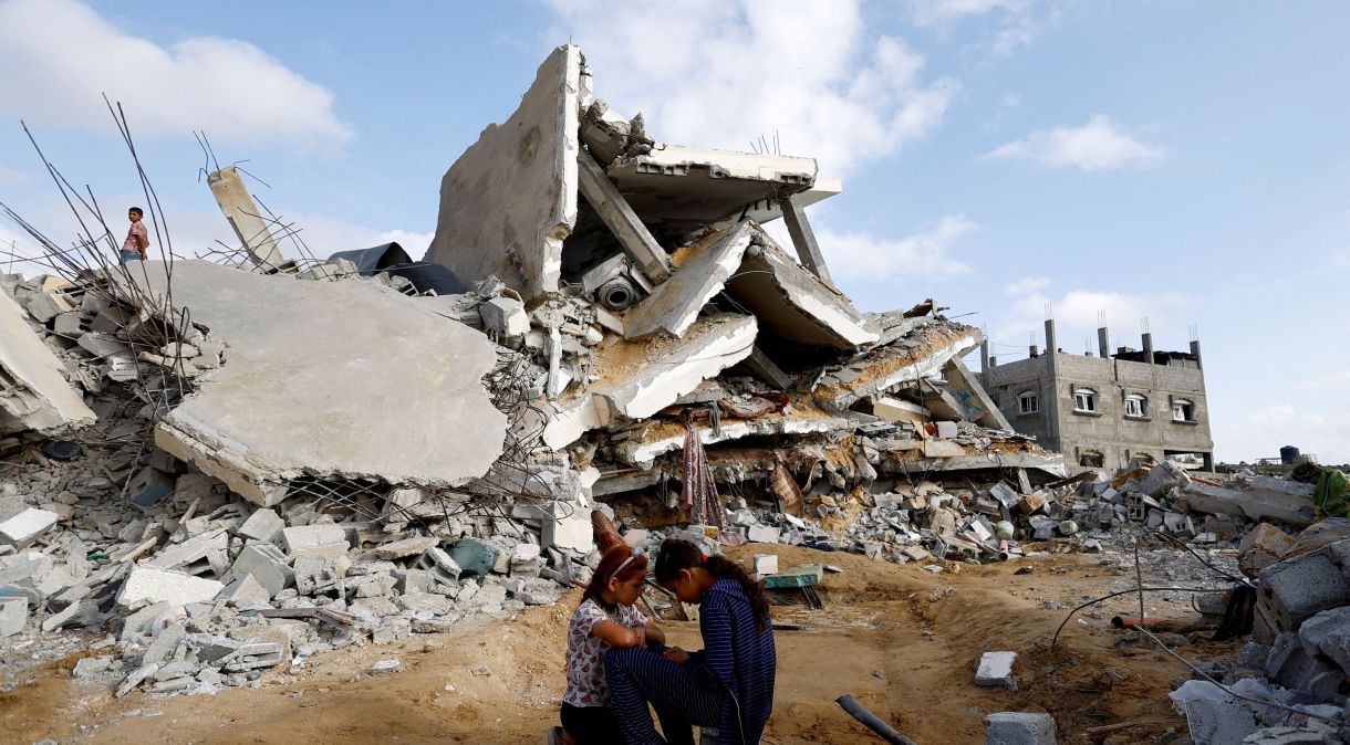 Crianças palestinas sentam-se perto de casa demolida por um ataque israelense em Rafah, no sul da Faixa de Gaza